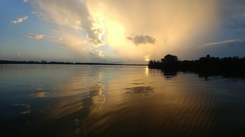A serene lake at sunset, with golden clouds reflecting on the water's surface and a calm atmosphere.