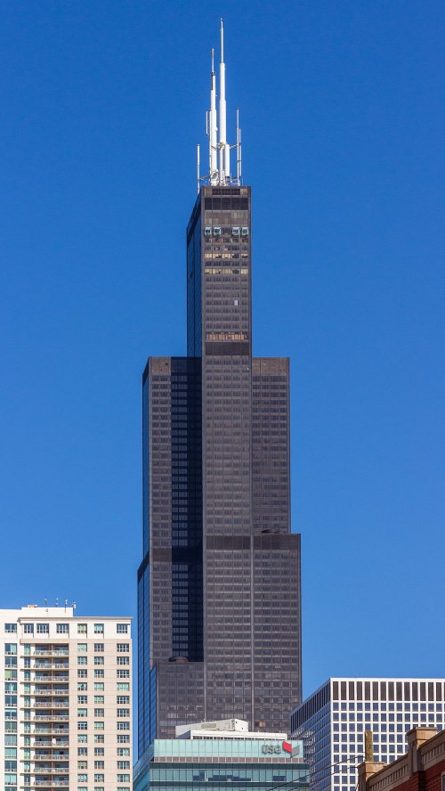 The Willis Tower, a tall black skyscraper, stands against a clear blue sky, showcasing its iconic design.