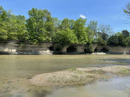 A serene river scene with lush green trees and rocky cliffs under a clear blue sky.