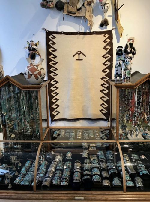 Display of Native American jewelry and crafts, featuring a woven textile and various turquoise pieces in a glass case.