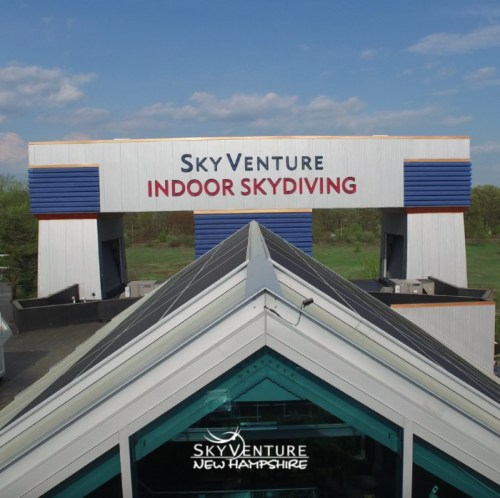 Aerial view of SkyVenture Indoor Skydiving building in New Hampshire, featuring a blue sky and green landscape.