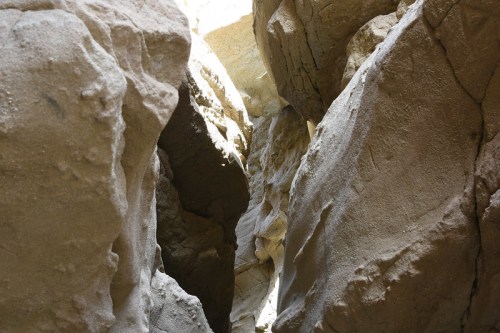 Narrow canyon walls of light-colored rock, illuminated by sunlight filtering through the top.