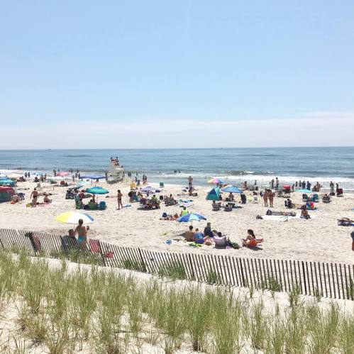 A sunny beach scene with people relaxing under umbrellas, playing in the sand, and enjoying the ocean waves.