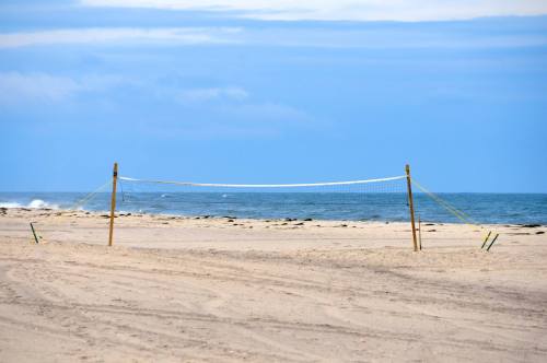 A sandy beach with a volleyball net set up near the calm ocean under a blue sky.