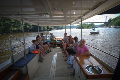 A group of people sitting on a boat, enjoying a scenic river view with another boat in the background.