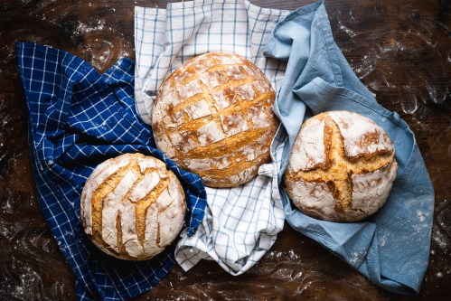 Three round loaves of bread on checkered cloths, resting on a wooden surface dusted with flour.