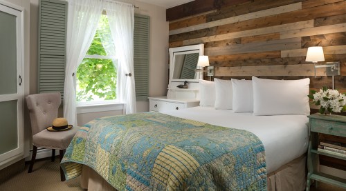 Cozy bedroom with a wooden accent wall, a bed with a colorful quilt, and natural light from a window.