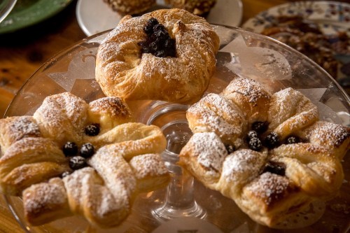 Three pastry flowers with powdered sugar and dark filling, displayed on a glass cake stand.