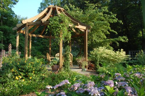 A wooden gazebo surrounded by lush greenery and colorful flowers in a serene garden setting.