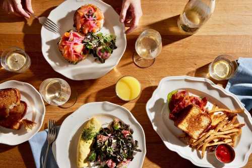 A table set with three plates of food, glasses of wine, and a bottle, featuring brunch dishes and a toast.