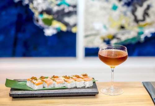 A plate of sushi with salmon on a leaf, accompanied by a cocktail in a glass, set against a colorful abstract background.