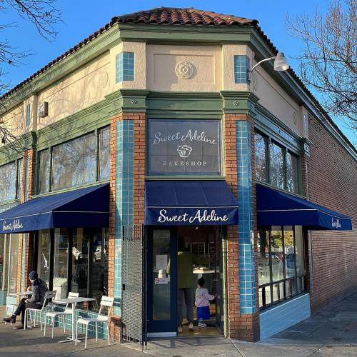 Exterior of Sweet Adeline Barbershop, featuring blue awnings and a welcoming entrance, with people outside.