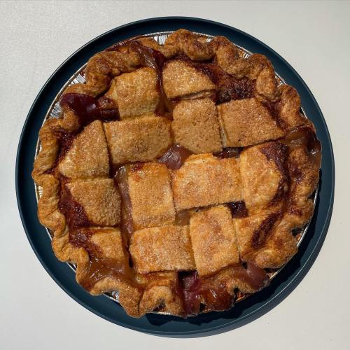 A freshly baked pie with a golden crust, topped with sugar and cut into squares, resting on a dark blue plate.