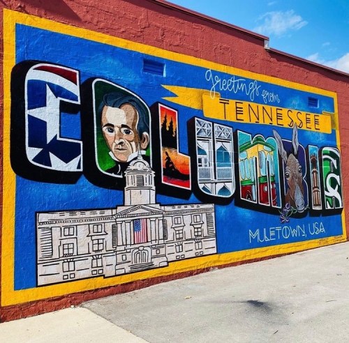Colorful mural reading "Greetings from Columbia, Tennessee" featuring local landmarks and a portrait.