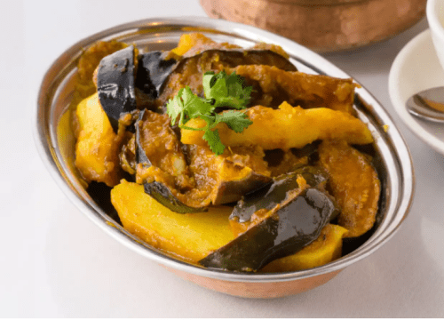 A silver bowl filled with a colorful vegetable dish featuring pumpkin and eggplant, garnished with fresh cilantro.