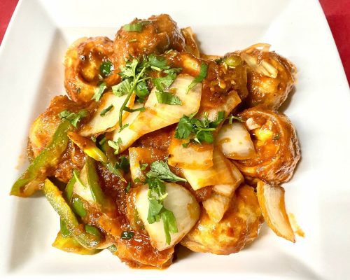 A plate of spicy dumplings topped with green peppers, onions, and cilantro in a rich sauce.