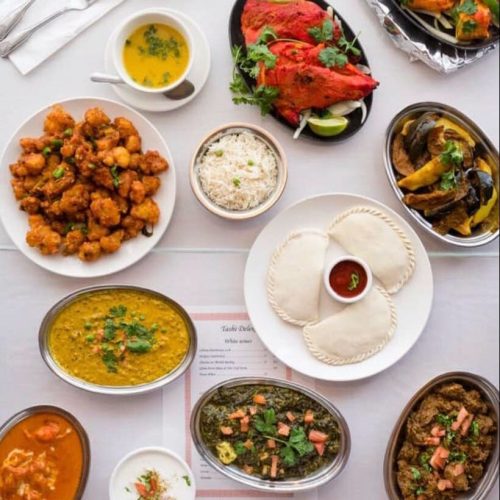 A vibrant spread of Indian dishes including curries, rice, bread, and appetizers, garnished with herbs.