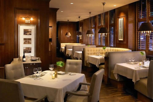 Elegant restaurant interior with wooden decor, cozy booths, and tables set for dining under soft lighting.