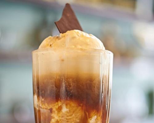 A tall glass filled with layered coffee, ice cream, and topped with a piece of chocolate.