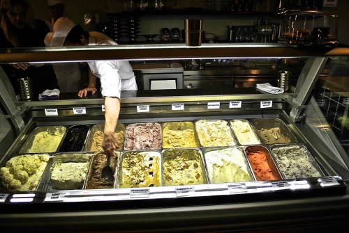 A display of various ice cream flavors in a shop, with a server scooping from a container.