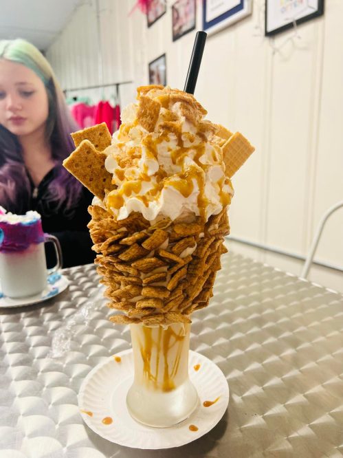A tall ice cream sundae topped with whipped cream, graham crackers, and caramel sauce, served in a glass.