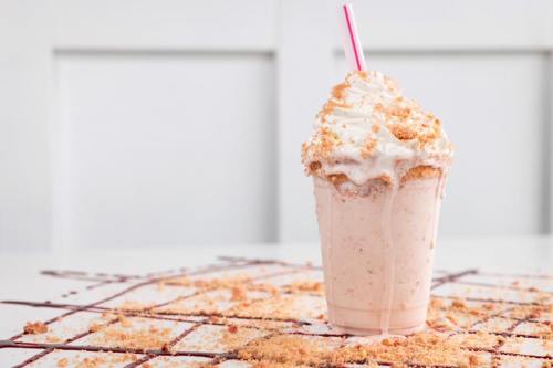 A creamy milkshake topped with whipped cream and cookie crumbs, with a pink straw, on a table with chocolate drizzle.