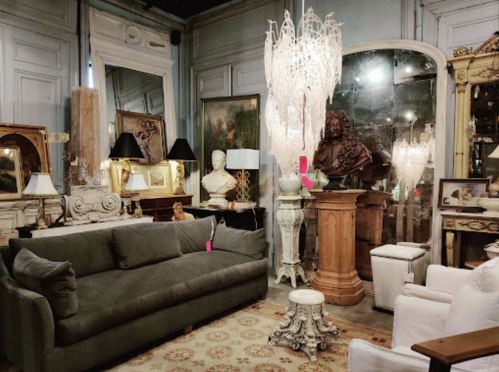 A cozy vintage interior featuring a green sofa, ornate decor, a chandelier, and various antique furnishings.
