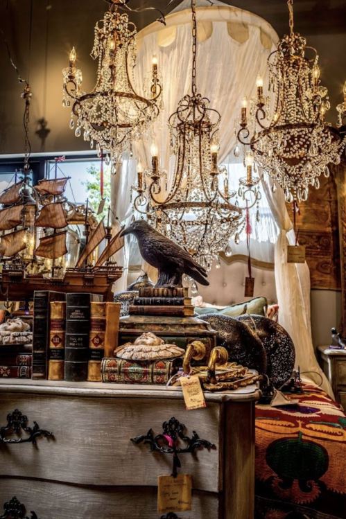 A cozy interior featuring ornate chandeliers, vintage books, decorative items, and a ship model on a stylish table.