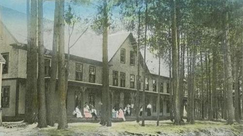 Historic building surrounded by tall trees, with people in vintage clothing gathered on the porch.