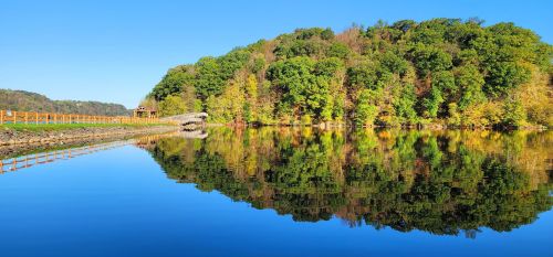 A serene lake reflecting a lush green hillside under a clear blue sky.