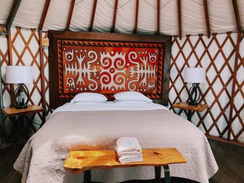 Cozy yurt interior featuring a double bed, decorative wall art, and wooden furniture with lamps.