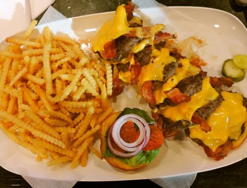 A plate featuring a stacked cheeseburger with bacon, melted cheese, and a side of crispy fries.