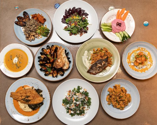 A variety of colorful dishes arranged on plates, including seafood, salads, and grains, displayed on a table.