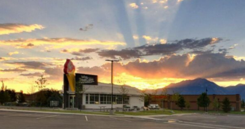 A colorful sunset behind a building with mountains in the background, casting rays of light across the sky.