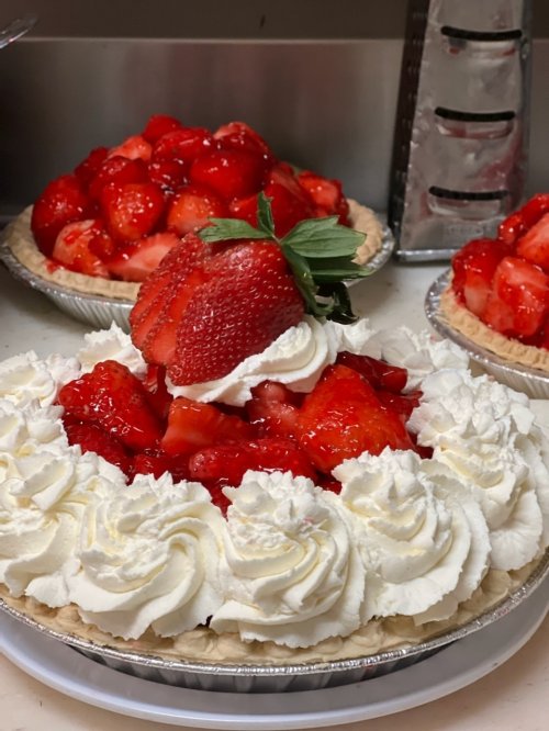 Three strawberry pies, one topped with whipped cream and fresh strawberries, sit on a countertop.