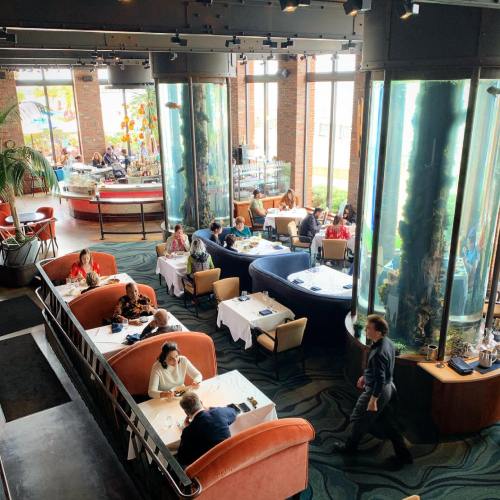 A stylish restaurant with large aquariums, featuring diners at tables and a waiter walking through the space.