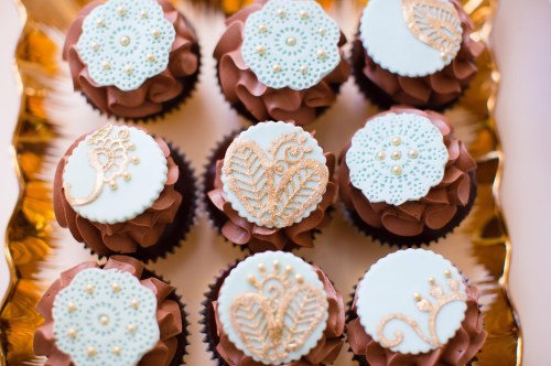 A tray of decorated chocolate cupcakes with light blue and gold floral designs on top.