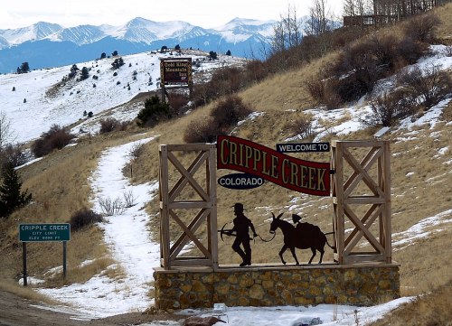 Welcome sign for Cripple Creek, Colorado, with mountains in the background and a silhouette of a miner and a mule.