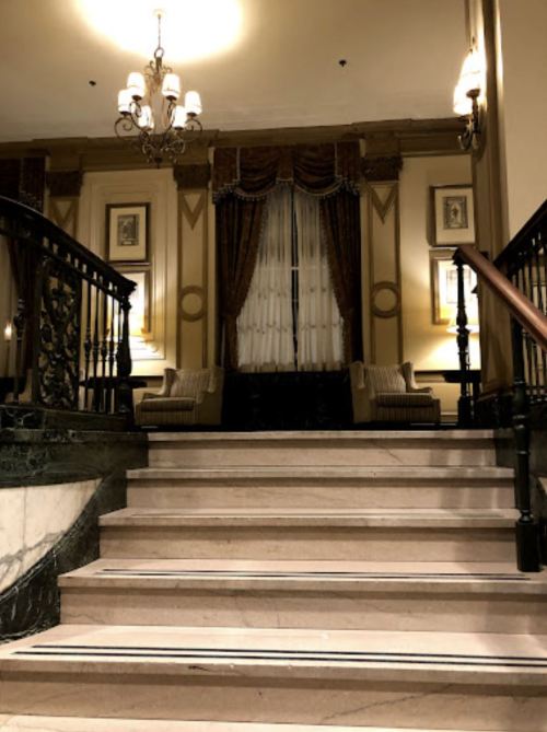 Elegant staircase leading to a well-decorated lobby with plush seating and ornate chandeliers.