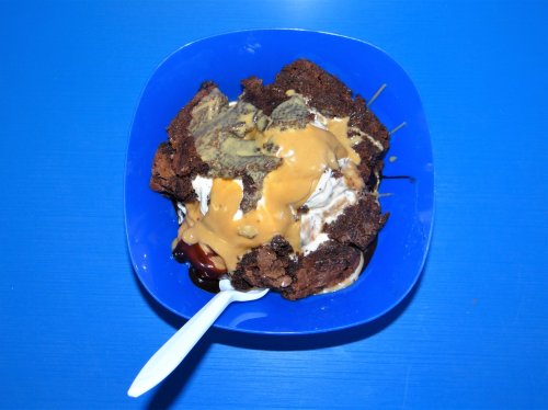 A blue bowl filled with ice cream, chocolate cake, peanut butter, and chocolate syrup, topped with a spoon.