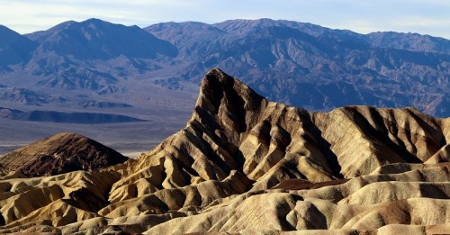 A rugged mountain landscape with layered, colorful rock formations under a clear sky.