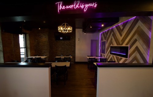Interior of a restaurant featuring a neon sign, modern decor, and a cozy atmosphere with tables and a fireplace.