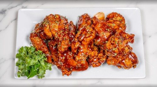 A plate of glazed chicken wings garnished with herbs, served alongside a small portion of leafy greens.