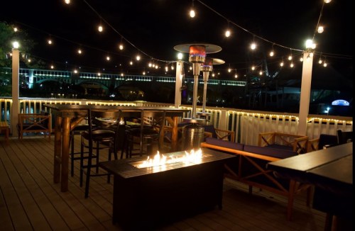 Cozy outdoor dining area at night, featuring string lights, a fire pit, and wooden furniture.