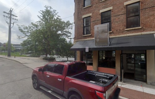 A red pickup truck parked in front of a brick building with a sign reading "130" and a black awning.
