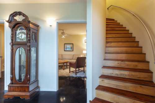 A wooden staircase leads to a cozy living area, with a vintage grandfather clock in the foreground.