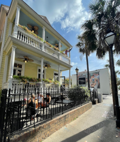 A charming yellow house with balconies, surrounded by palm trees, and outdoor seating on a sunny day.