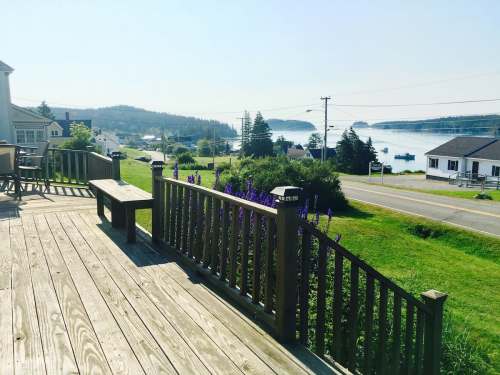 A wooden deck overlooks a scenic view of a bay, with houses and greenery in the background under a clear sky.