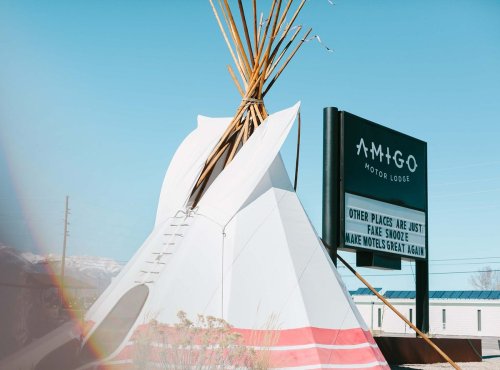 A teepee structure next to a sign for Amigo Motor Lodge, with a clear blue sky in the background.