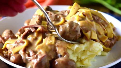 A plate of creamy beef stroganoff served over mashed potatoes, with a fork digging into the dish.